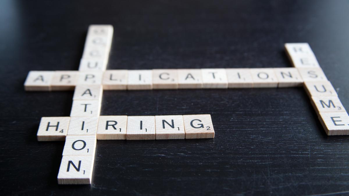 Photo of Scrabble tiles on a dark wood surface with the words OCCUPATION, APPLICATION, RESUME, and HIRING
