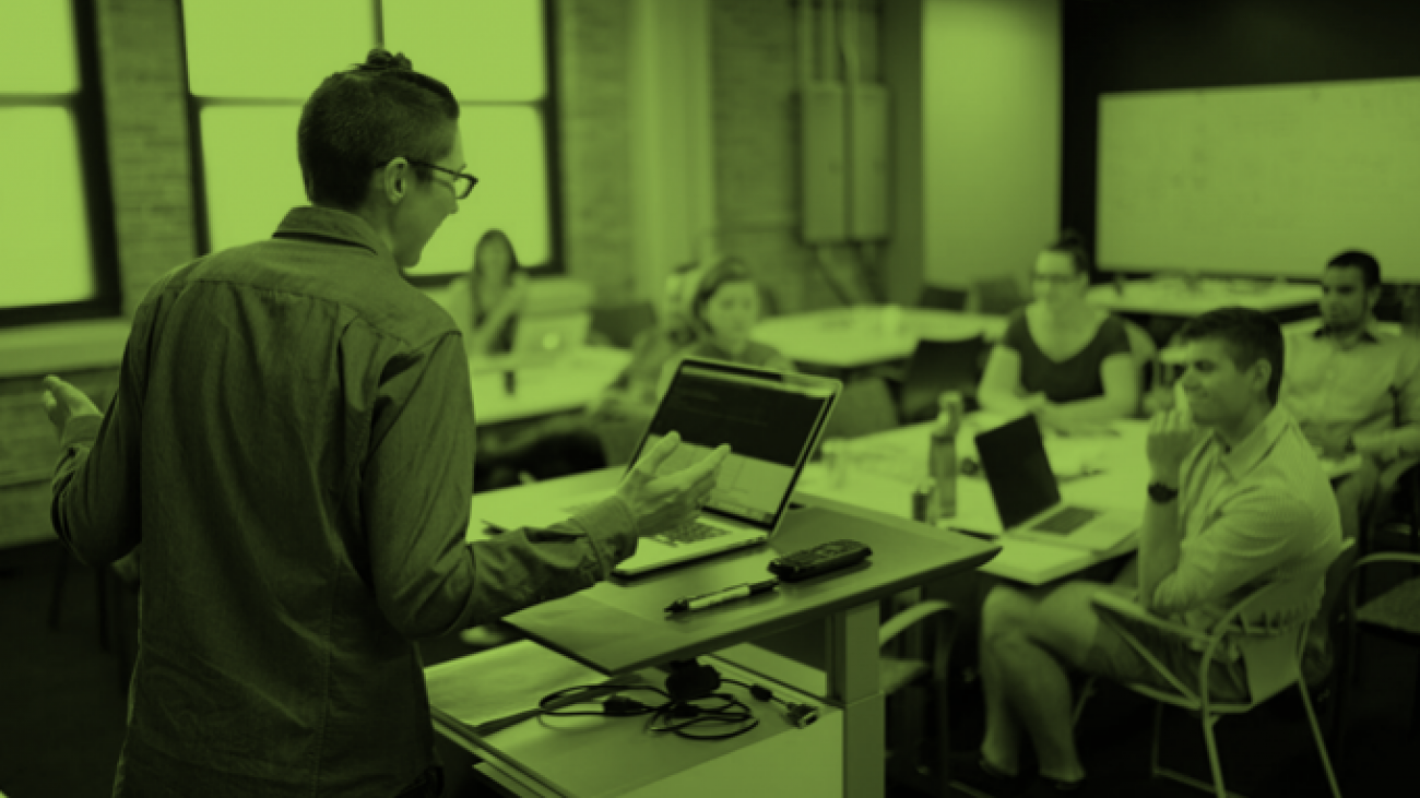 Photo of person speaking at a podium in front of people sitting at a table