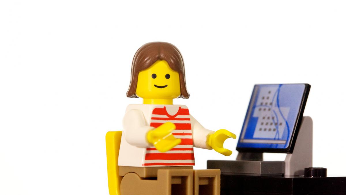 Smiling Lego minifig sitting at Lego computer workstation