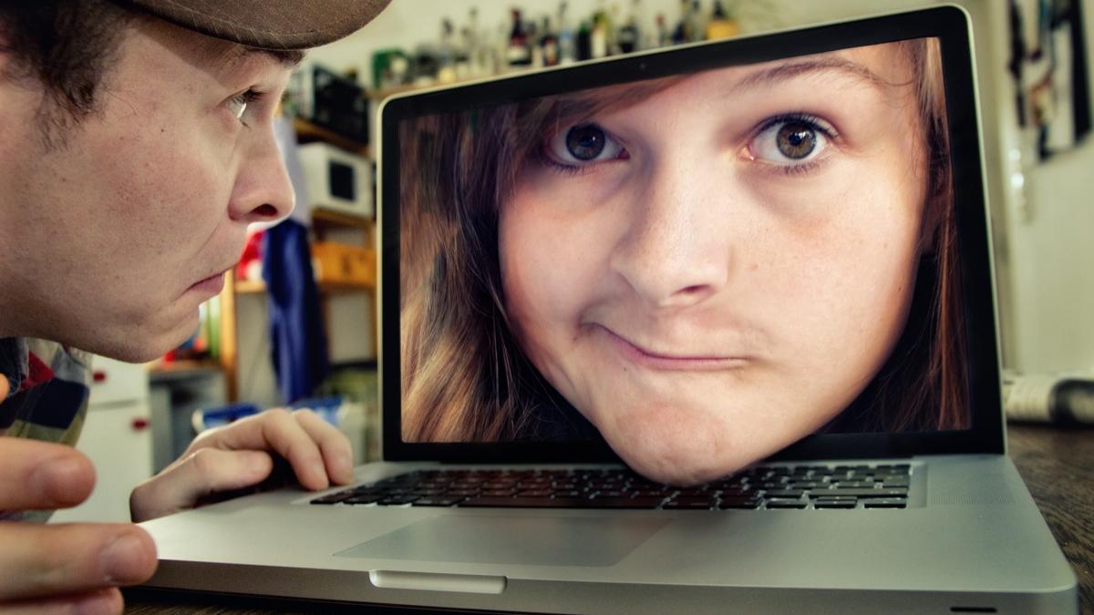 Photo of a man quizzically looking at a laptop with a woman's face popping out of the screen.