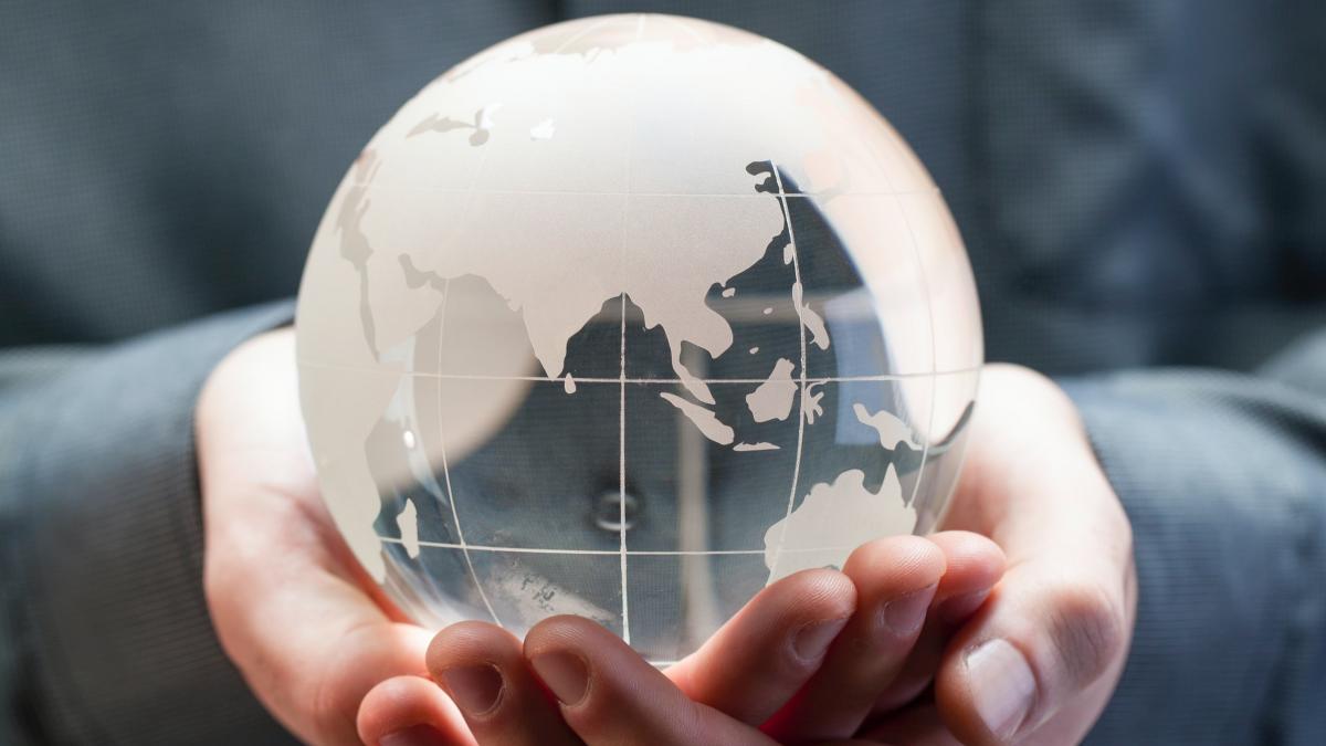 Photo of a person holding a glass globe of the Earth in their hands.