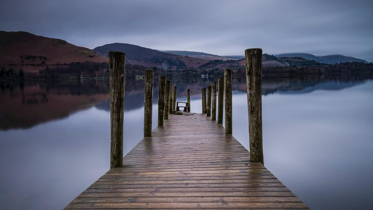 Photo of a brown wooden dock on a body of water with hills in the background