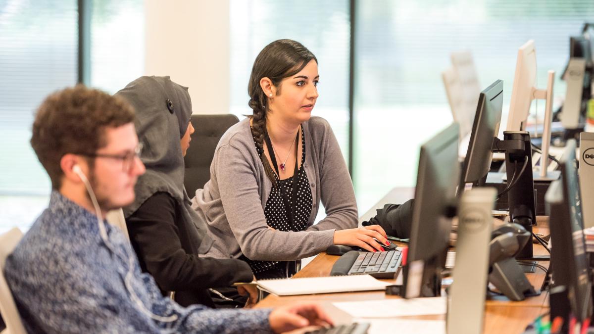 Two women, one man sitting at computers and working together