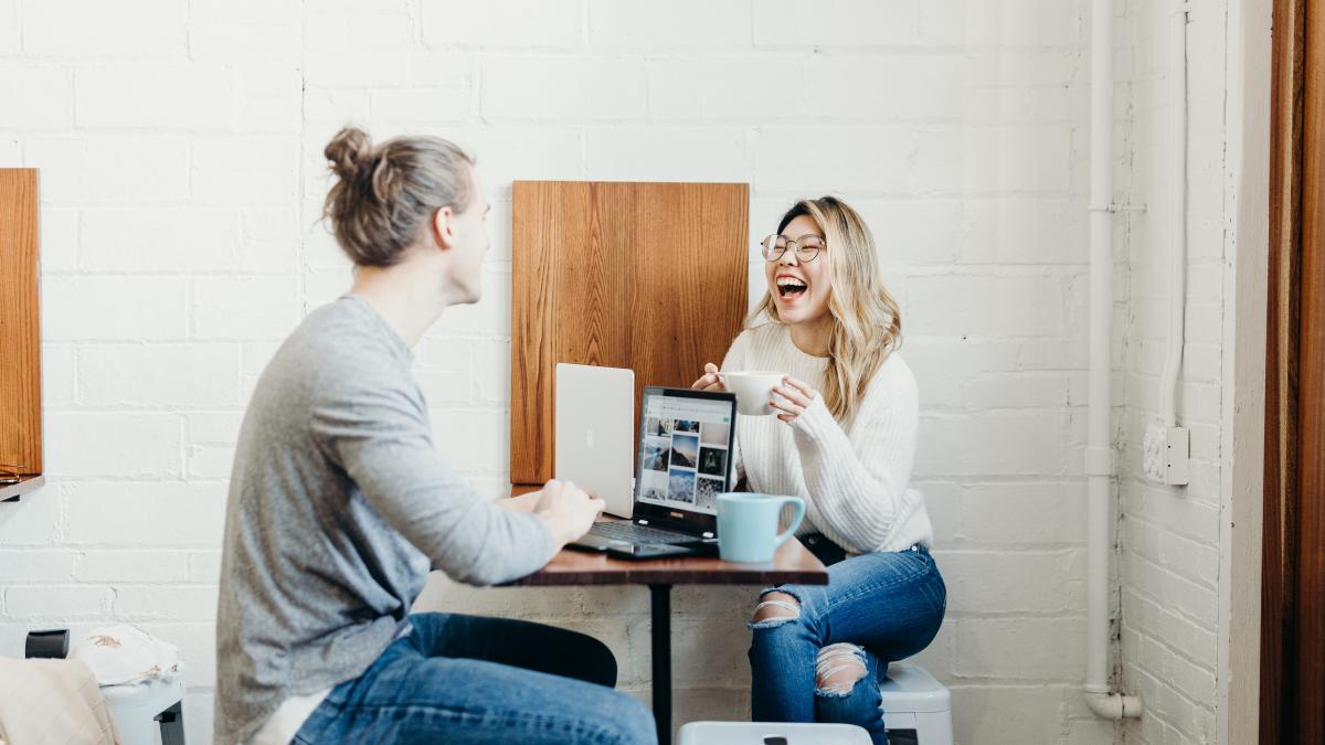 Woman holding a coffee cup and smiling at a man sitting opposite her at a coffee shop