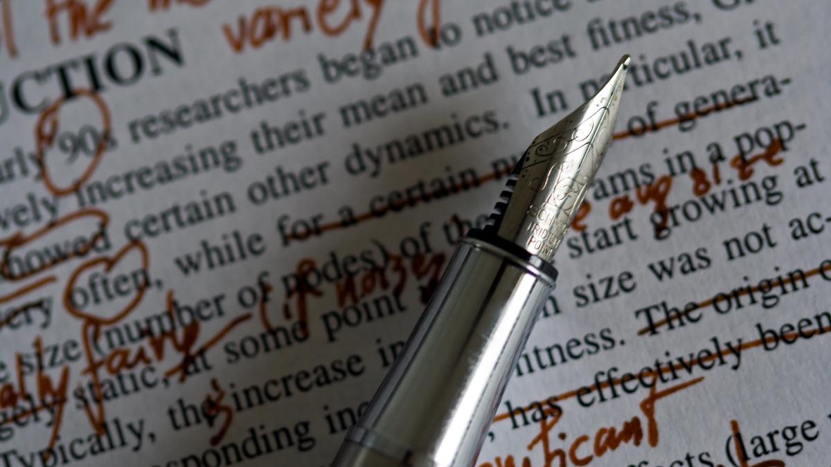 Close-up photo of the tip of a silver fountain pen with a page of edited text in the background