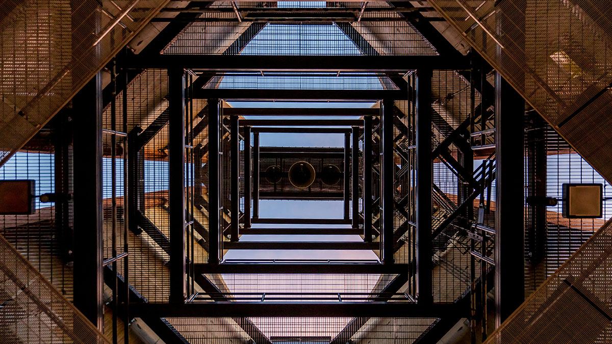 A view looking up at the underside of a building with a large bell in the center.