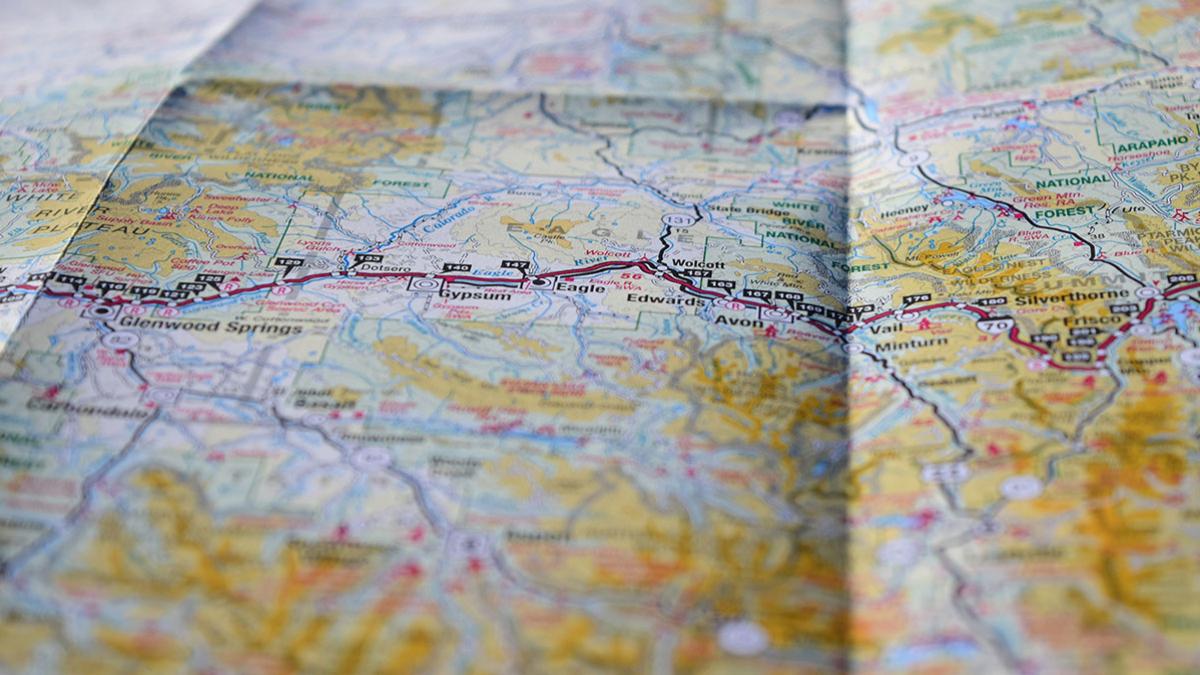 Asection of a road map showing various locations, routes, and landmarks. There are highways marked in black and red, with towns and cities such as Glenwood Springs, Gypsum, and Edwards labeled. Surrounding areas include natural features like national forests. The map is slightly folded, giving it a 3D texture.