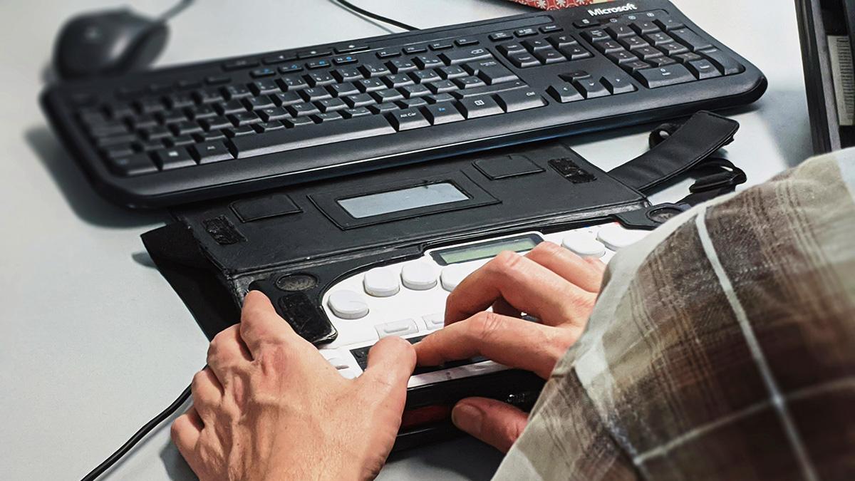 A person using a braille keyboard at a workstation