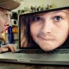 Photo of a man quizzically looking at a laptop with a woman's face popping out of the screen.