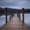 Photo of a brown wooden dock on a body of water with hills in the background