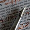 Close-up photo of the tip of a silver fountain pen with a page of edited text in the background